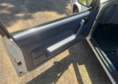 Driver's door is open and showing a blue door panel, black door handle, and black window crank.